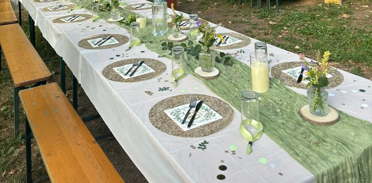 Lange, festlich gedeckte Tafel im Grünen mit Kerzen und Blumen