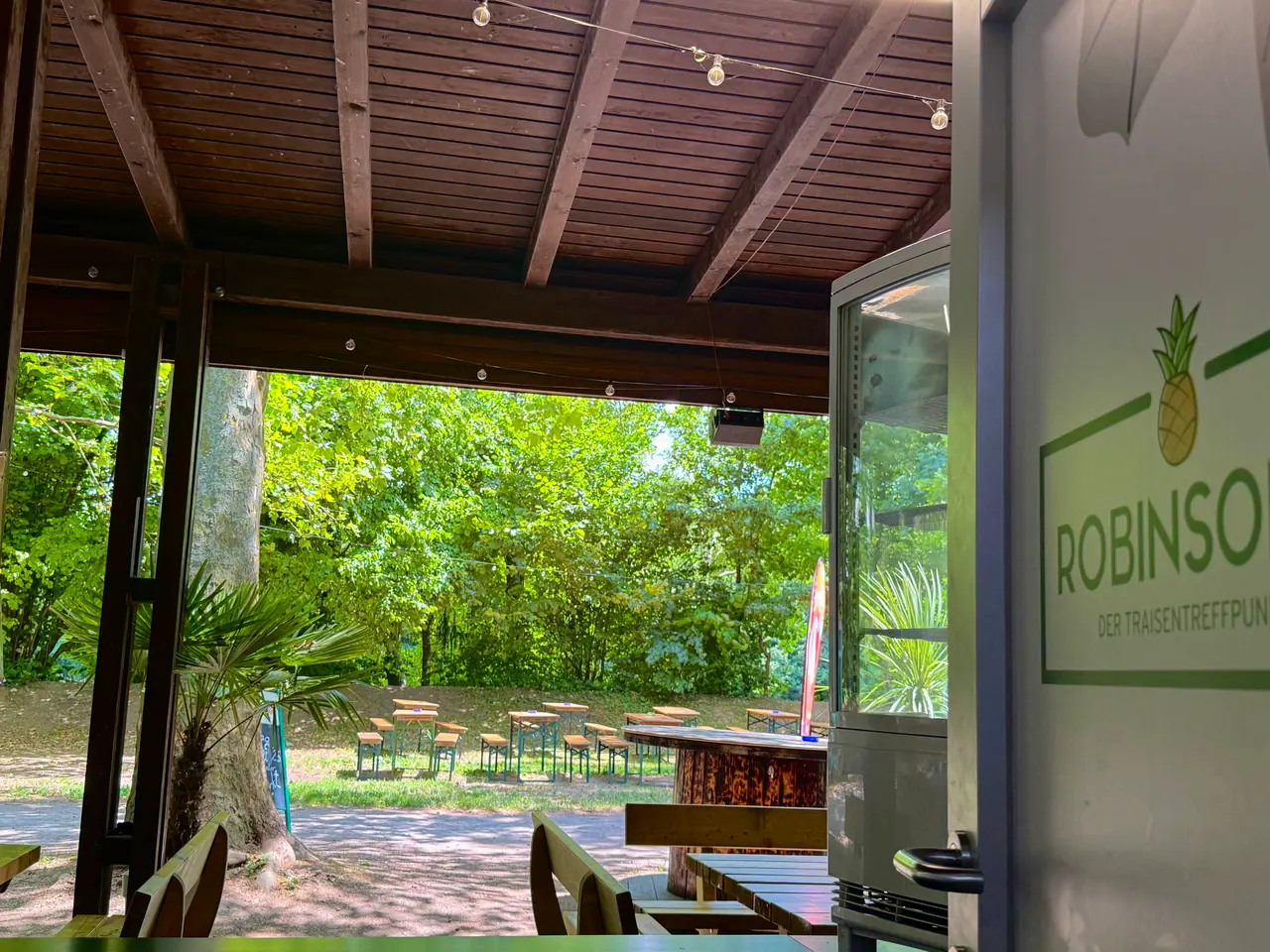 Blick aus dem überdachten Pavillon mit ROBINSON'S Schild in den grünen Garten
